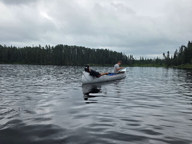 A loaded canoe gliding across a dark forest-lined lake