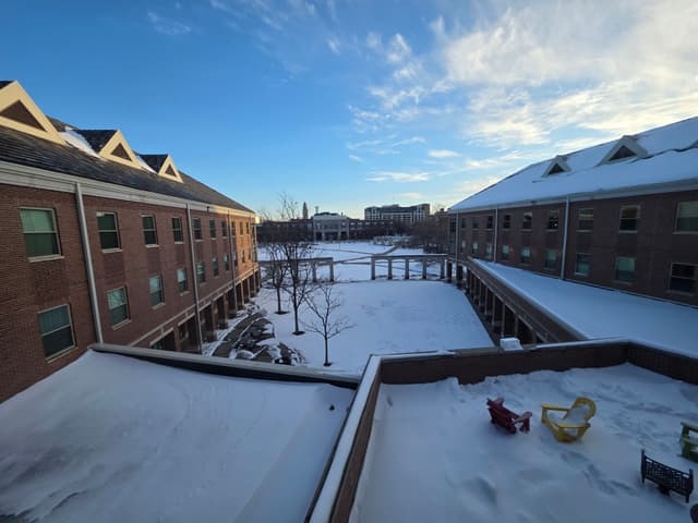 A snowy courtyard between brick residence halls under a blue sky
