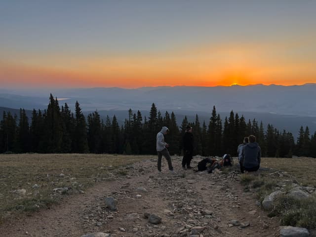 Friends watching the sun set from a high ridge