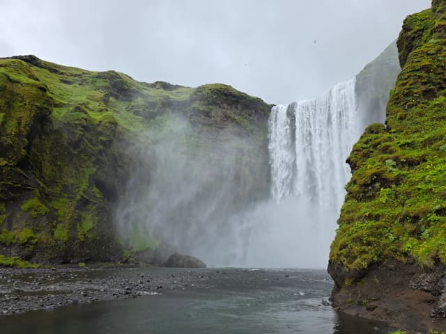 Skógafoss pouring into a misty green gorge
