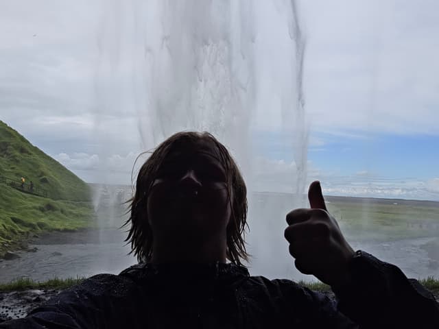 Finn silhouetted behind the curtain of Seljalandsfoss, thumbs up