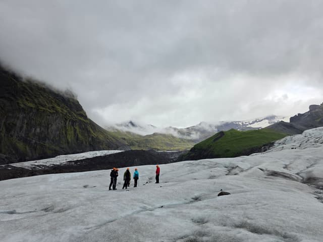 A small group roped up on a grey glacier under low clouds