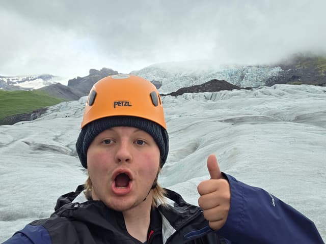 Finn in an orange helmet making a surprised face on the glacier