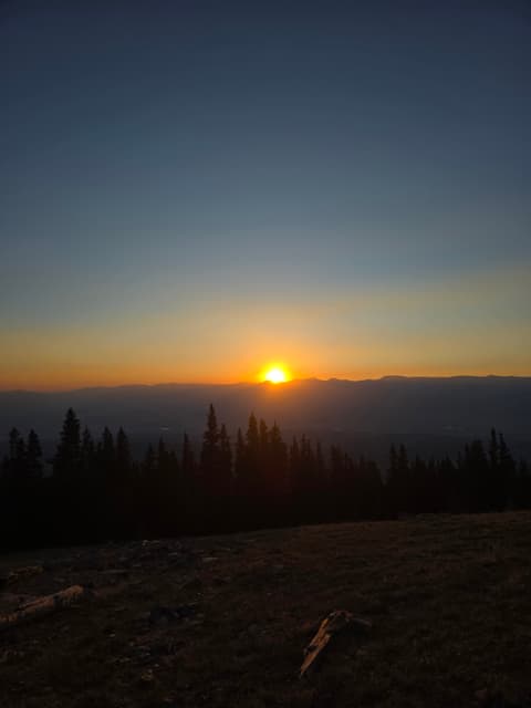 The sun rising over distant ridges above treeline