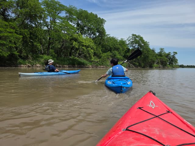Two kayakers paddling ahead on a wide brown river