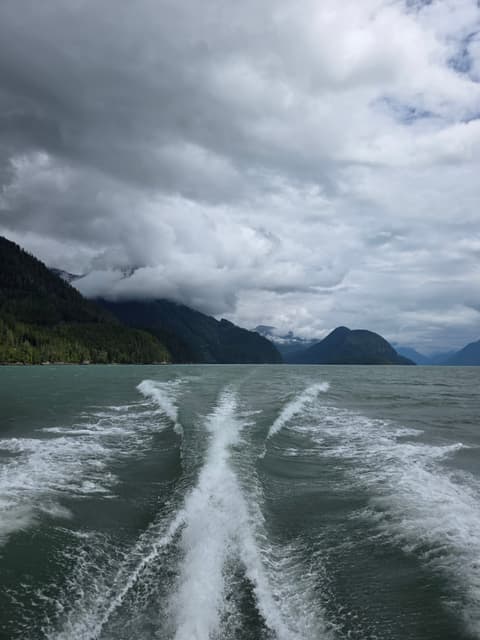 A boat wake trailing down a mountain-lined inlet