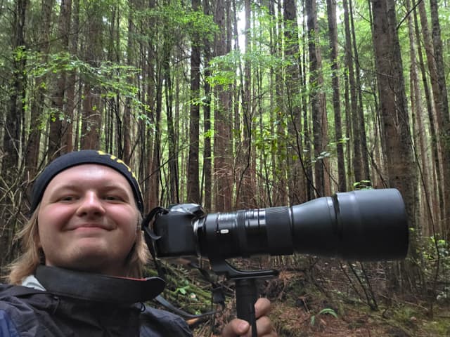 Finn grinning behind a long telephoto lens in the rainforest