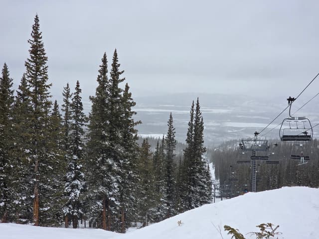 A chairlift above snowy pines and the valley below