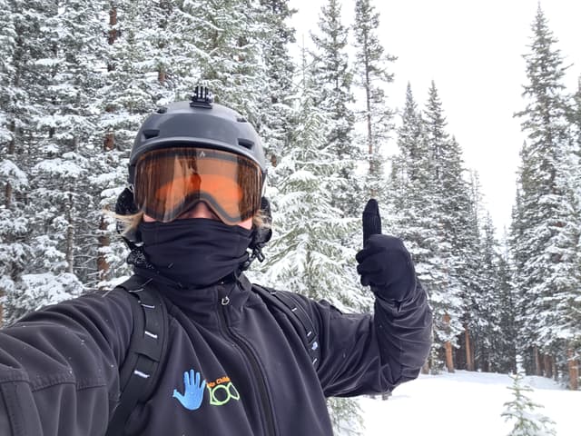 Finn in a helmet and goggles giving a thumbs up in snowy trees